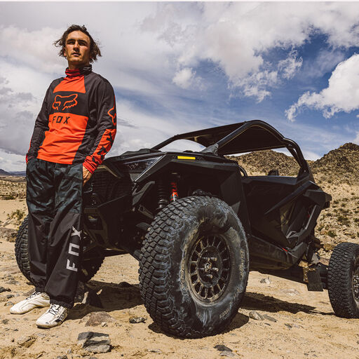 Man in red jersey standing his parked by a side by side