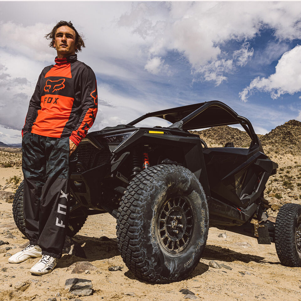 Man in red jersey standing his parked by a side by side